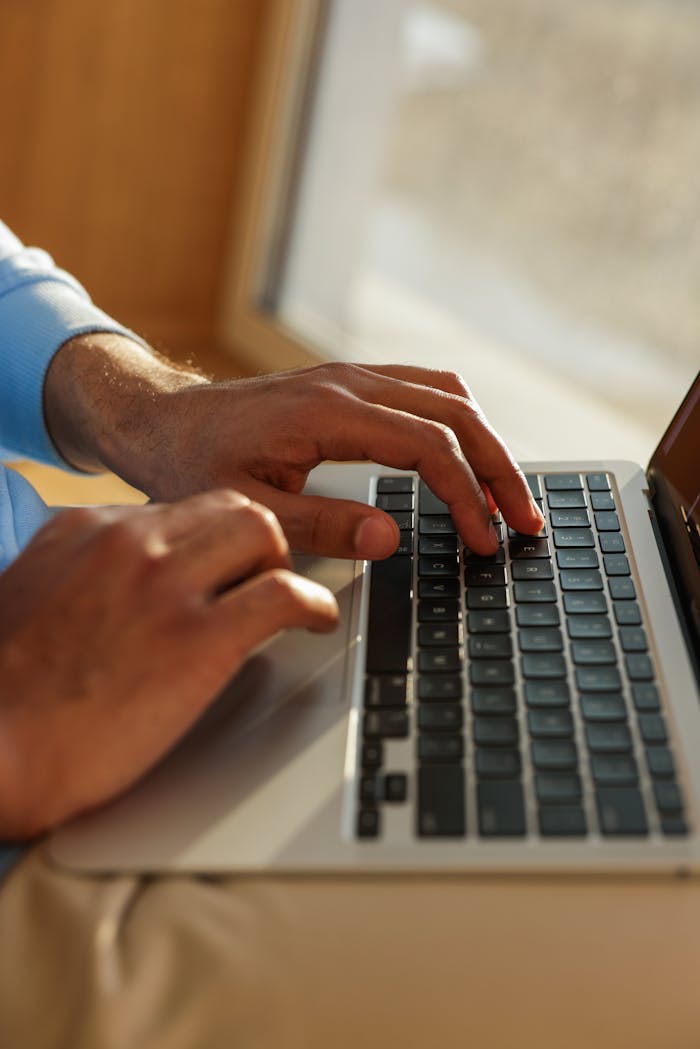 Close-up view of hands typing on a laptop, indoors. Focus on technology and work efficiency.